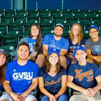 A group of nine gvsu tigers fans. 5 in the front row of seats and 4 in the back, all smiling